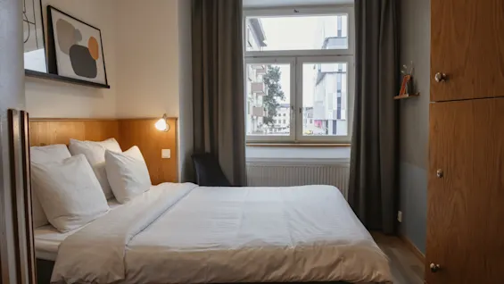 Mukava hotellihuone Home Hotel Uppsalassa siististi pedatulla sängyllä, ikkunalla kaupunkinäköalalla ja lämpimällä valaistuksella.