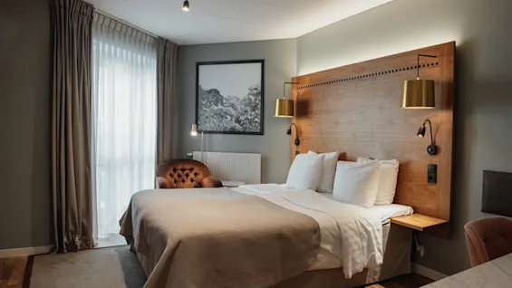 Et hyggeligt hotelværelse med en stor seng, sengegavl i træ og varm belysning, der indbyder til et behageligt ophold.