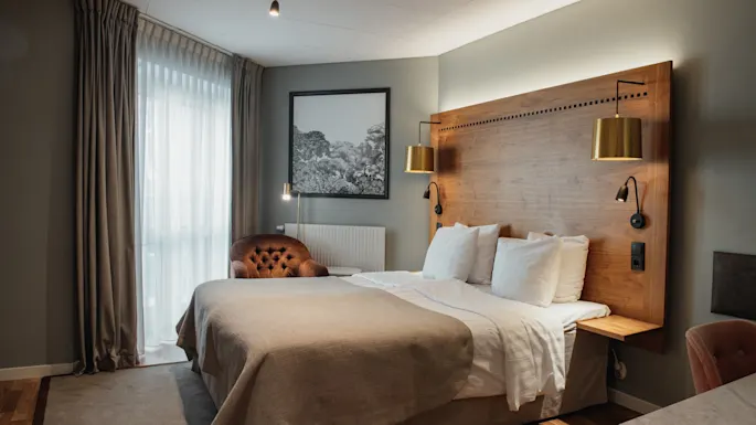 Et koselig hotellrom med en stor seng, sengegavl i tre og varm belysning, som inviterer til et komfortabelt opphold.