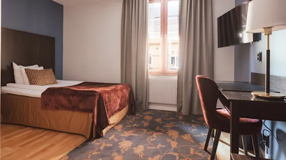 Et pent arrangert hotellrom med oppredd seng, skrivebord, stol og flatskjerm-TV. Det fremstår som koselig.