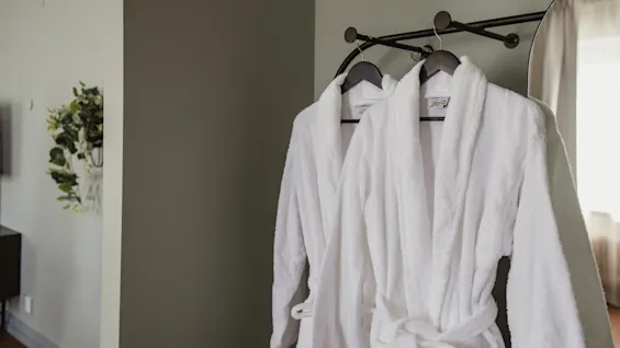 Två mjuka vita badrockar hänger redo att användas i ett bekvämt hotellrum, inbjudande till avkoppling och komfort.