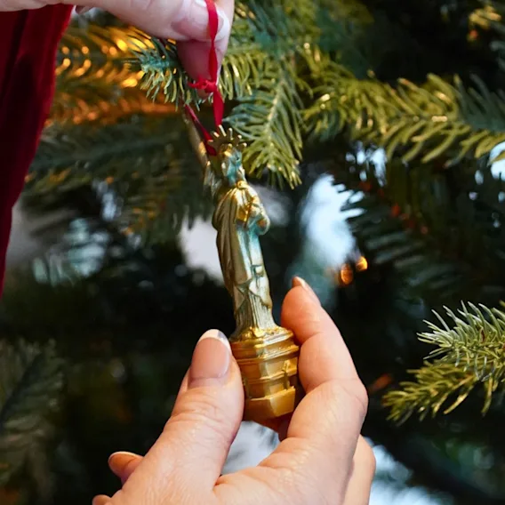 Händer som hänger upp en gyllene juldekoration i en grön julgran.