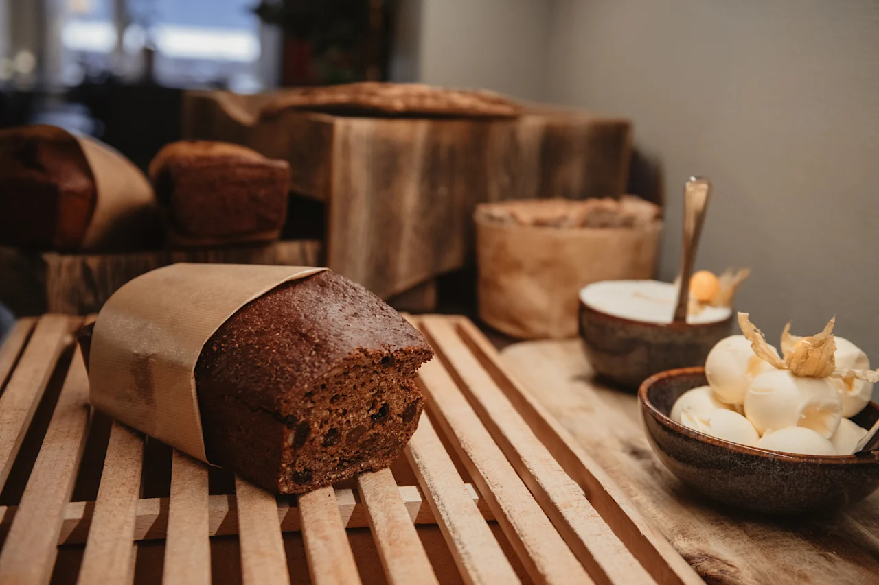 En rustik uppvisning av nybakat bröd och skålar med krämig efterrätt med fruktgarnering på en träyta.