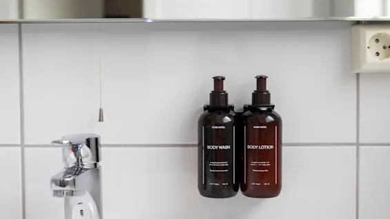 En ren badeværelsesdisk med en moderne vandhane og vægmonterede dispensere til BODY WASH og BODY LOTION.