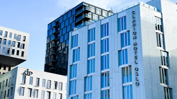 A modern building with blue-tinted windows displays the vertical text "CLARION HOTEL OSLO" in an urban skyline, next to another building with "KLP" logo.
