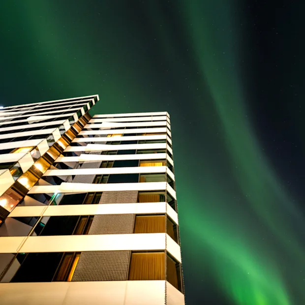 En modern hotellfasad upplyst på natten, med livfulla gröna norrsken som dansar över den mörka himlen ovanför.