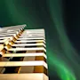 En modern hotellfasad upplyst på natten, med livfulla gröna norrsken som dansar över den mörka himlen ovanför.