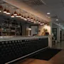 A stylish bar area with a long, dark tufted counter, shelves of bottles, and warm pendant lighting, leading to an open lounge.