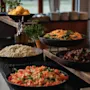 A vibrant buffet spread featuring fresh salads like shredded carrots with spinach, beet salad, and chopped tomatoes.