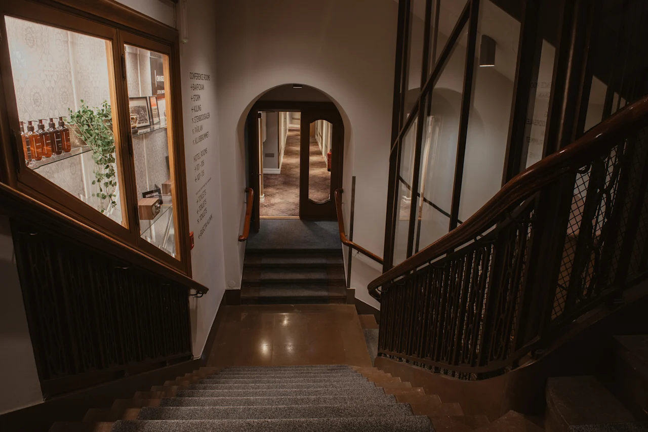 En hotelltrappa leder nedåt, med en monter och en katalog för hotellfaciliteter och rum. En välvd korridor väntar.