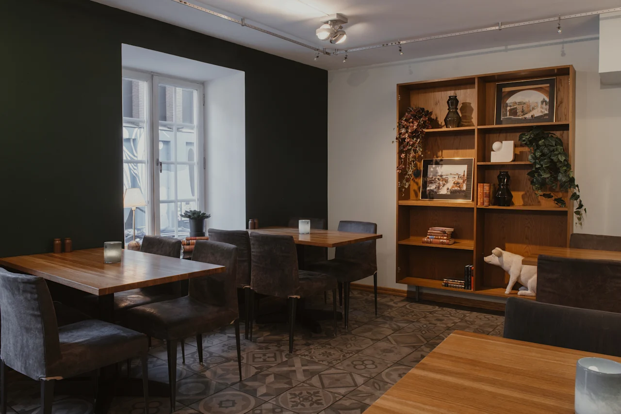 Mysig matplats med träbord, mörka stolar, ett stort fönster och en bokhylla. Home Hotel Grand, Helsingborg.