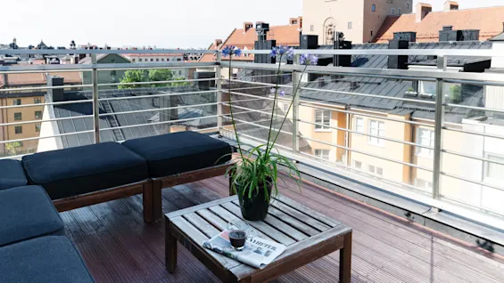 En uteplats med möbler och en växt, med utsikt över stadslandskapet.