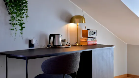 En bekväm skrivbordsplats med vattenkokare, varm lampa och en vintage radio, mot en vägg med en hängande växt.