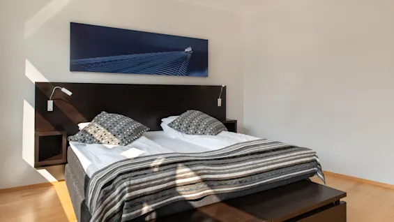 Et lyst og indbydende hotelværelse med en komfortabel seng, mørk sengegavl, stribet tæppe og et bådkunstværk.