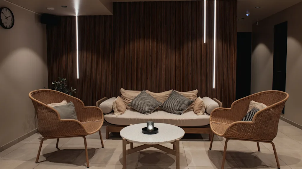 A cozy lounge area at Home Hotel Uppsala with a sofa, two armchairs, and a coffee table, featuring warm lighting and a wooden accent wall.