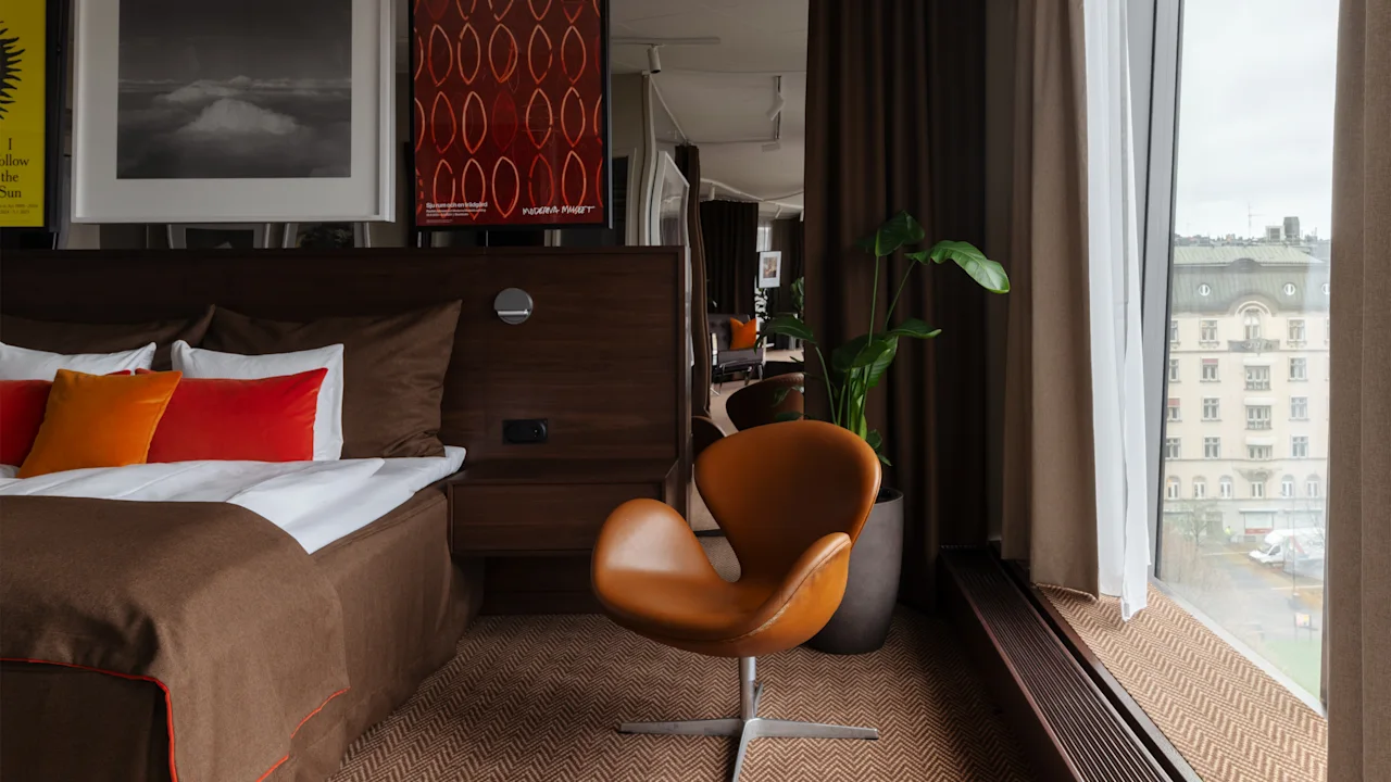 Clarion Hotel Sign Tukholmassa, Stratum Suite by Bernadotte ja Kylberg. Moderni huone sängyllä, tuolilla ja kaupunkinäkymällä. Seuraan aurinkoa.