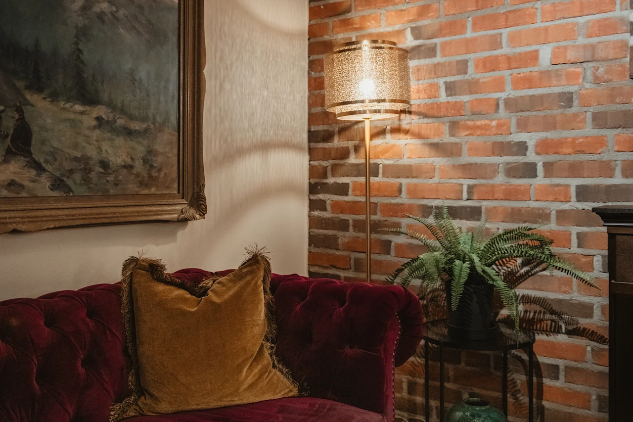 Ett varmt och inbjudande rum med en plyschröd soffa, en glödande lampa mot en tegelvägg och en livlig ormbunke.