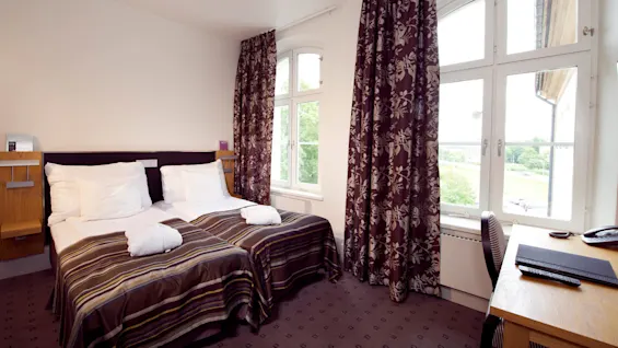 Two single beds with striped covers in a room with a window overlooking green trees.