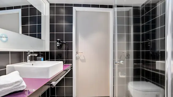 A modern bathroom with a white sink, a towel, a toilet, and a shower with glass door; black and white tiled walls.