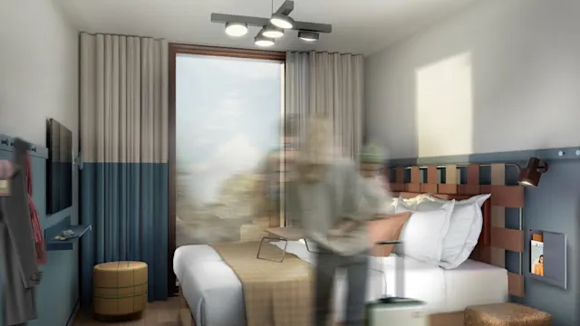 A person placing items on a bed in a modern hotel room with minimalistic decor, featuring a large window, teal and beige accents, wall-mounted TV, and overhead lighting.