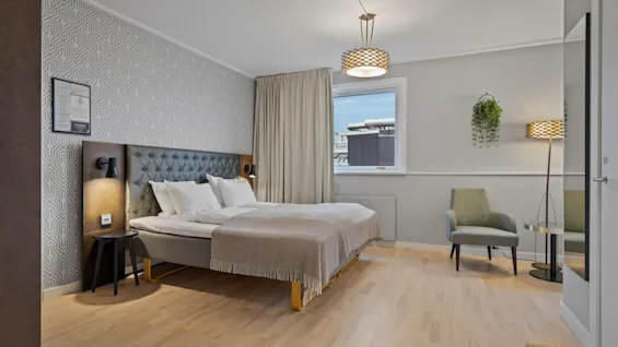 Ett modernt och inbjudande hotellrum med en bekväm säng, en mysig fåtölj och ett fönster med utsikt över staden.