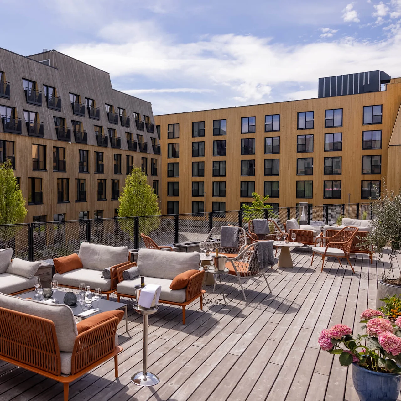 Utomhus loungeområde på en trätrall med moderna möbler, omgivet av byggnader under en klar himmel.
