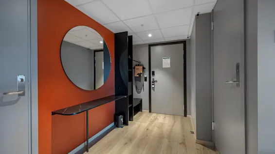 En moderne hotellromsinngang på Comfort Hotel Porsgrunn med et rundt speil, et lite bord og lyst tregulv.