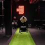 Mann skyver vektet slede på grønt underlag i treningsstudio. "ONE MORE REP" i neonlys på svart vegg. Omgivende utstyr inkluderer benker og vekter.