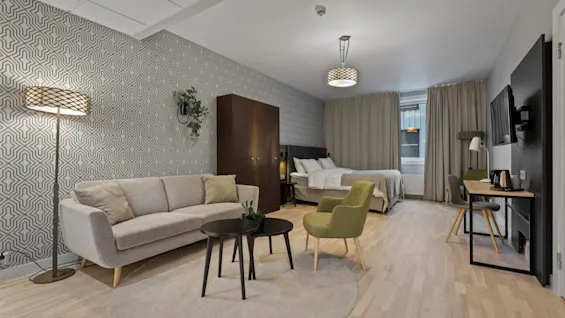 Ett modernt hotellrum med en bekväm vardagsrumsdel med soffa och stolar, en mysig säng och en funktionell arbetsplats.