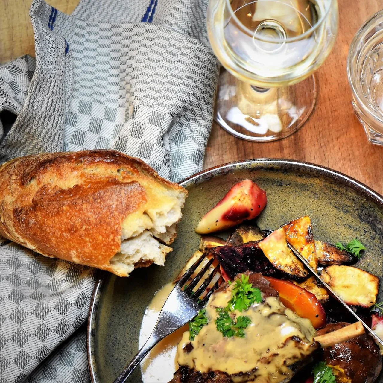 Et gourmetmåltid med biff og ovnsstekte grønnsaker på en tallerken, ledsaget av vin og vann på et trebord.