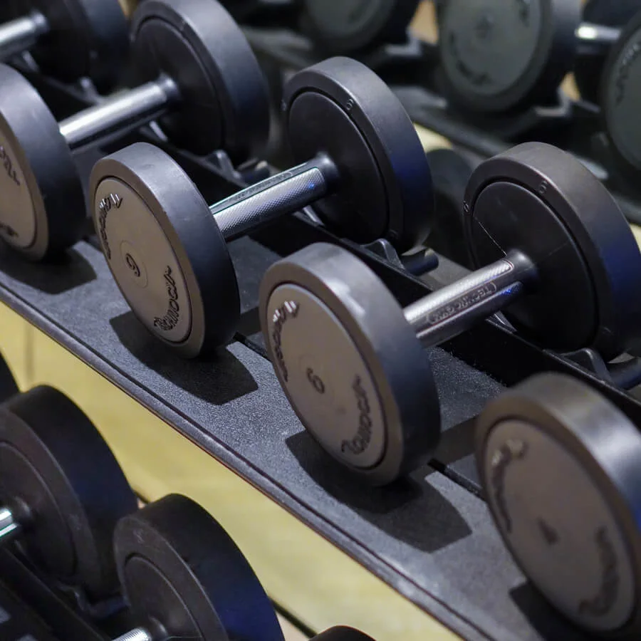 Hantlar ligger prydligt på ett ställ, i linje med en spegel som reflekterar dem, i ett gym. Text på hantlarna: "Escape."
