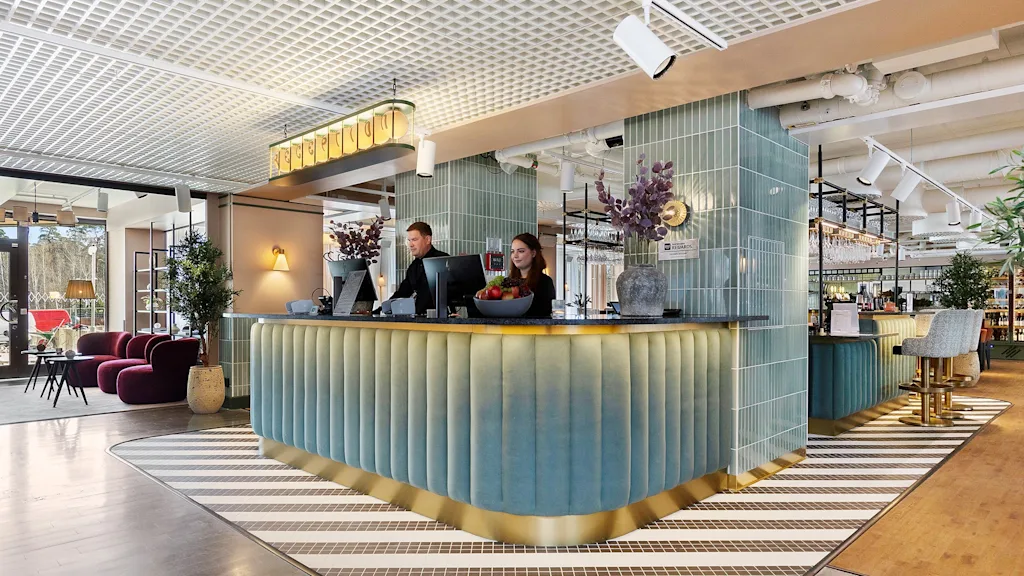To ansatte som står bak en moderne hotellresepsjon og ønsker gjester velkommen.
