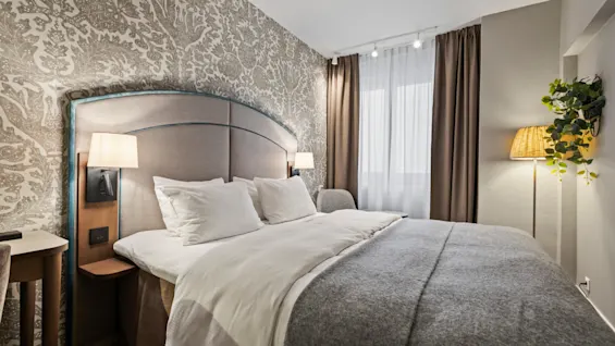 A cozy hotel room with a large bed, patterned wallpaper, and warm lighting, perfect for relaxation.