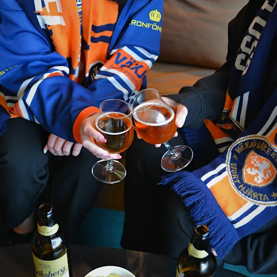 Två hockeyfans i lagtröjor skålar med ölglas över lite snacks