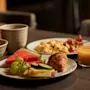 Et dejligt morgenmadsbord på et træbord, med frisk frugt, en croissant, røræg, bacon og juice.
