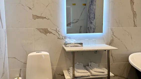 Moderni kylpyhuone marmorikuvioiduilla seinillä, hehkuvalla peilillä ja wc-istuimella. Junior Suite Comfort Hotel Linköping Cityssä.