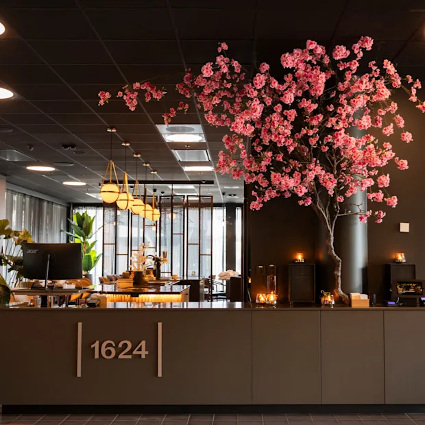 En moderne hotellobby med en resepsjon som viser '1624', et stort rosa kirsebærtre og stilig belysning.