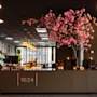 En moderne hotellobby med en resepsjon som viser '1624', et stort rosa kirsebærtre og stilig belysning.