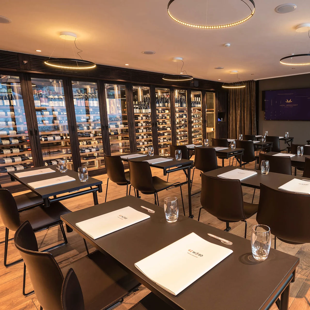 Rows of tables with notebooks and glasses in a conference room, surrounded by wine racks and wooden floors. Notebook text: "GIN NORD". Screen text: "HOTEL UNFORGET - Events & Entertainment".