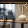 A cozy indoor scene with a vase of dried pampas grass on a table, set against the warm glow of a modern fireplace.