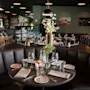 Et koselig restaurantinteriør med mørkebrune båser og bord dekket for bespisning, med et barområde i bakgrunnen.