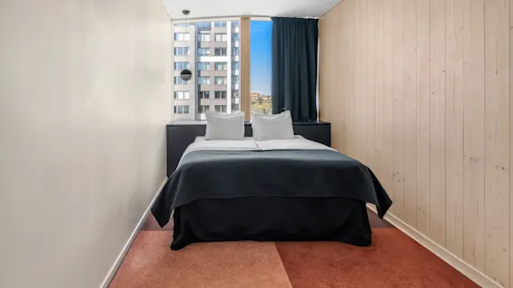 Et moderne og indbydende hotelværelse med komfortabel seng, stort vindue med byudsigt og et varmt, tofarvet tæppe.