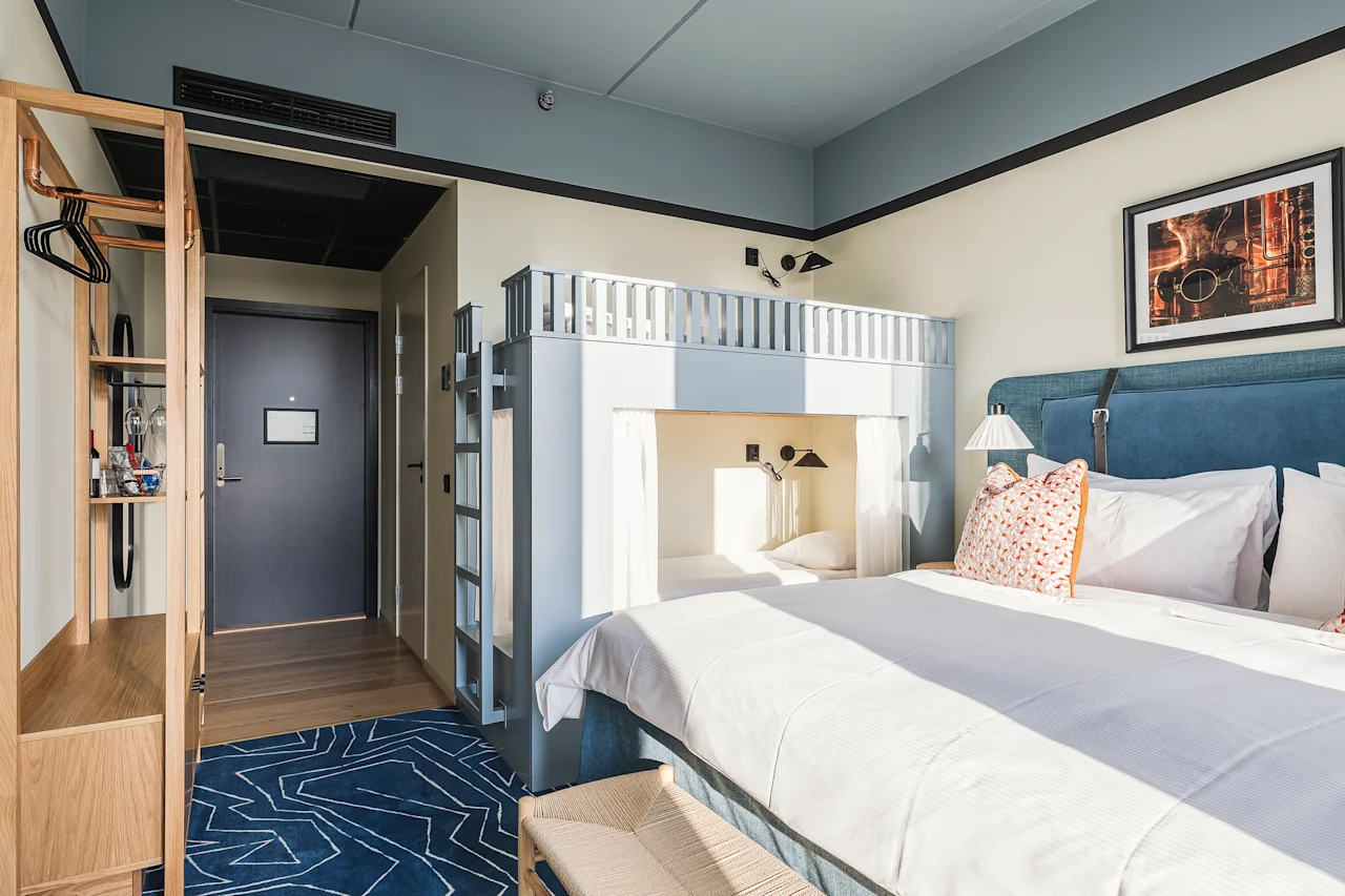 Et lyst og moderne hotelværelse på Hernö Gin Hotel med en stor seng og en køjeseng, perfekt til et familieophold.