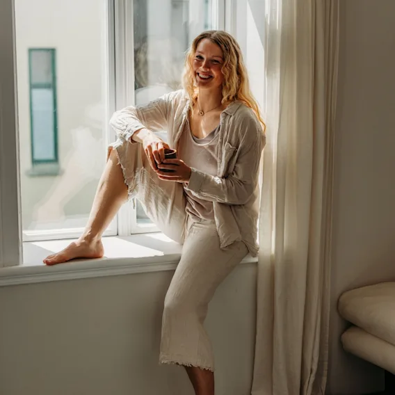 Solveig Skutvik sitter i en solfylt vinduskarm med en liten kopp.
