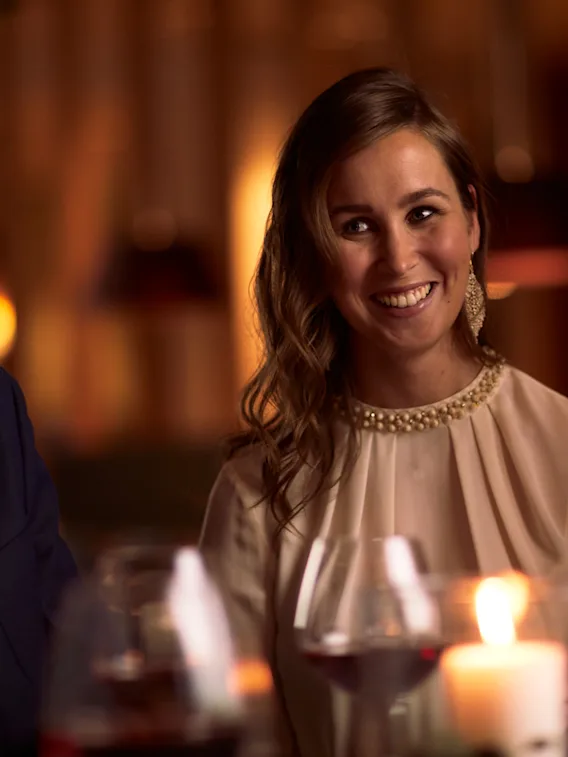 En mann og kvinne i pyntede klær smiler og ler sammen rundt et levende lys under en restaurantmiddag.