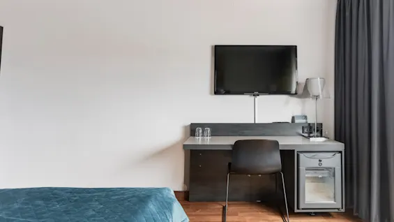 A modern hotel room featuring a comfortable bed, a functional desk area with a chair, a wall-mounted TV, and a mini-fridge.