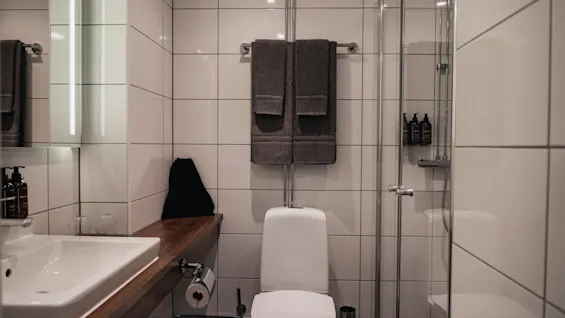 Ett rent och modernt badrum med handfat, toalett och dusch, med fräscha handdukar och toalettartiklar lättillgängliga.