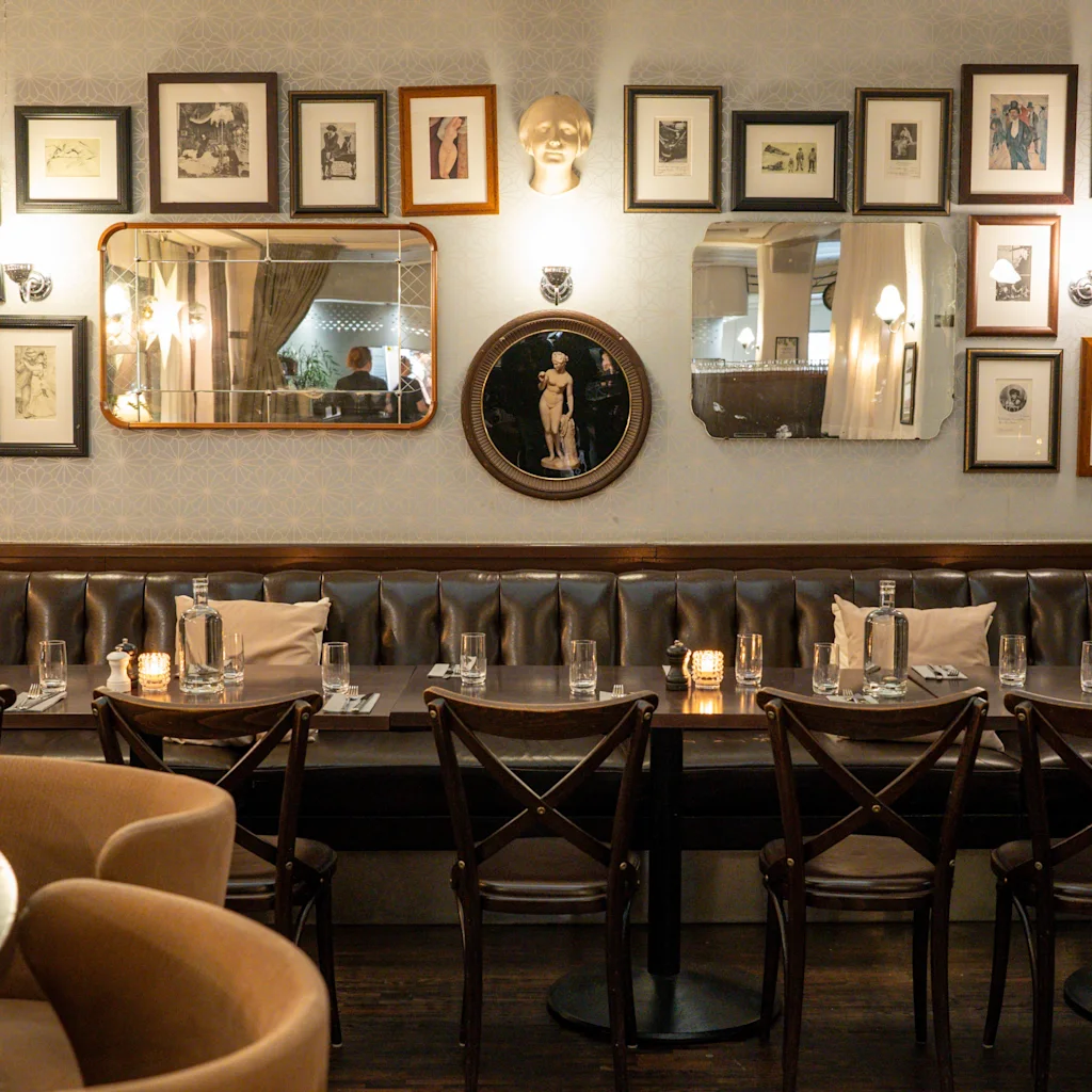 Hyggelig restaurant på Clarion Hotel Winn, med læderbænk, dækkede borde og en væg med indrammet kunst og spejle.