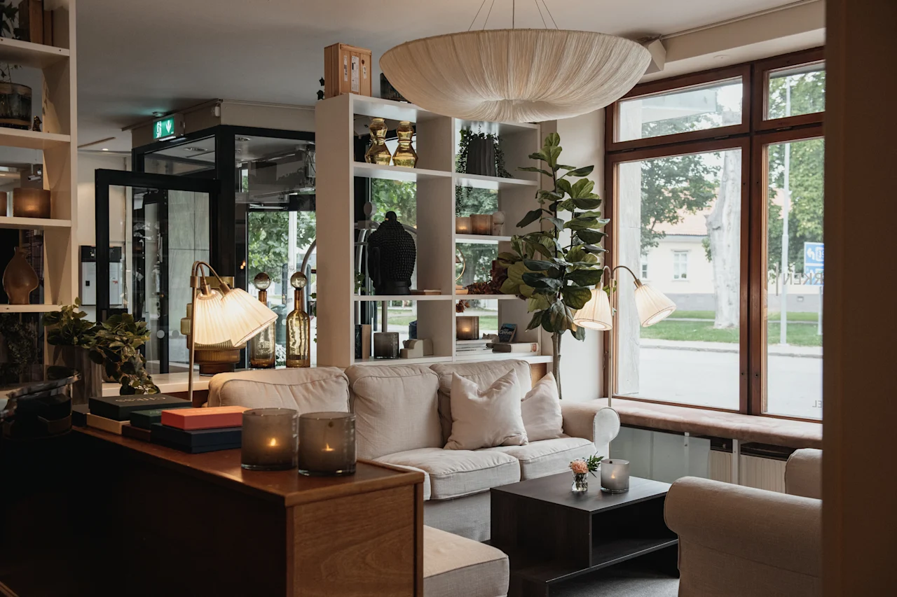 A warm and inviting hotel lobby with comfortable seating, a bookshelf, and a large window overlooking a street. EXIT sign visible.