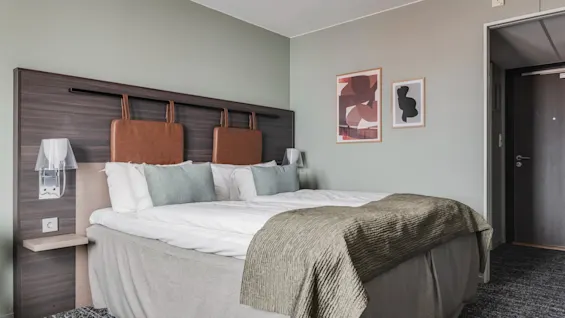 Et moderne hotellrom med en stor seng, abstrakt kunst på veggen og en koselig atmosfære.